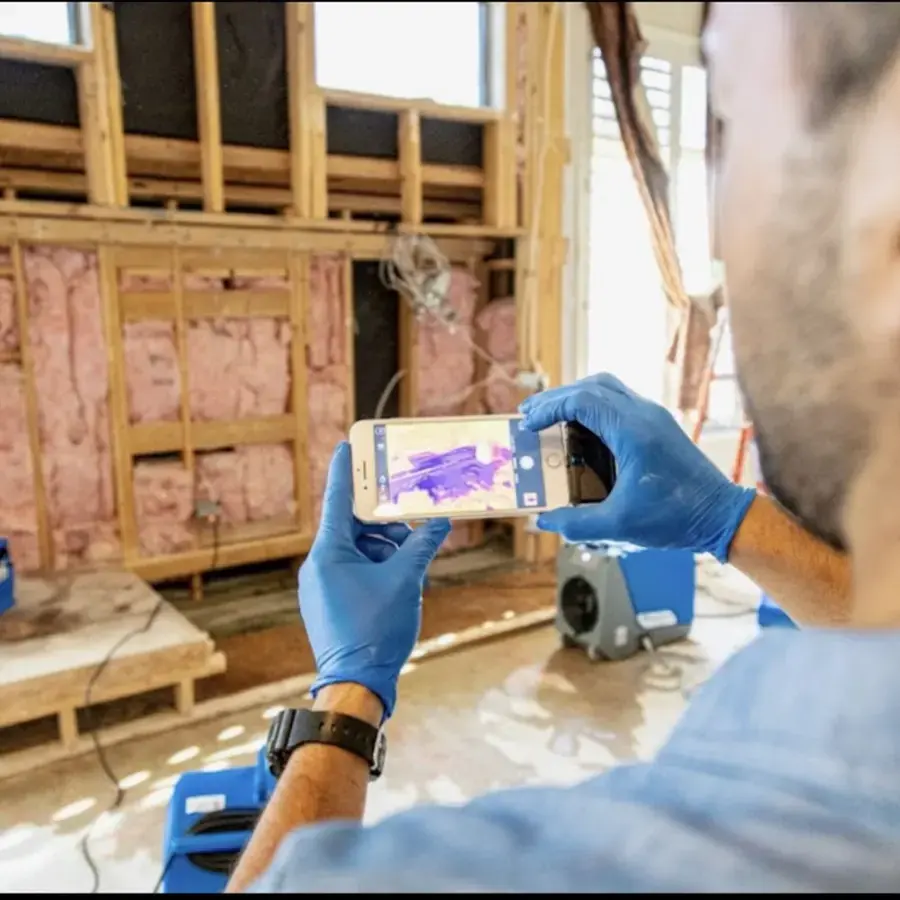 Technician using a thermal camera to map moisture in open wall framing during a Weatherford dry-out